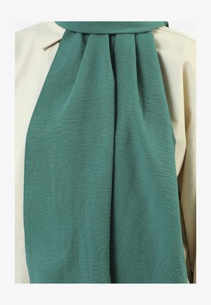 Green textured scarf draped over a light-colored shirt, with soft, flowing fabric and subtle wave patterns throughout.