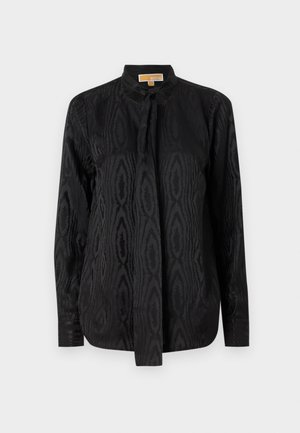 Zwarte blouse van soepel materiaal, met een subtiel ton-sur-ton patroon, lange mouwen, een staande kraag en een striksluiting in de nek.