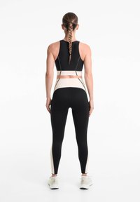 Crop top de sport noir avec une bande beige clair contrastante, associé à un legging taille haute avec des panneaux latéraux beige et un tissu texturé.