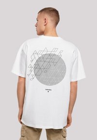 White cotton t-shirt featuring a large gray circle with geometric black line patterns on the back. Loose fit with short sleeves.