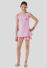 Débardeur en coton rose avec un col rond et un logo de fleur orange ; associé avec un short rayé rouge, rose et blanc.