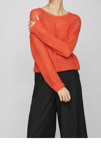 Ljust orange, stickad tröja med lös, öppen väv och bred halsringning. Matchad med svarta byxor med vid ben.