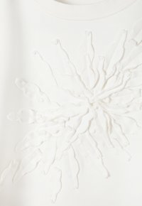 Felpa bianca con design floreale testurizzato al centro, realizzata in un materiale morbido con accenti di tessuto stratificati e allungati.