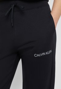 Zwarte joggingsbroek van een katoenmix, met een elastische tailleband met trekkoord, zijzakken en een wit logo op de dij.
