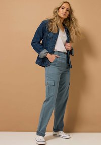 Jeansjacka, vit t-shirt och ljus teal cargo byxor med sidofickor. Enkla vita sneakers. Slät textur; avslappnad passform.
