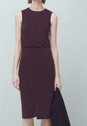 Robe sans manches bordeaux avec un design drapé, taille cintrée et ourlet jusqu'aux genoux. Tissu lisse avec une texture subtile. Blazer noir drapé sur le bras.