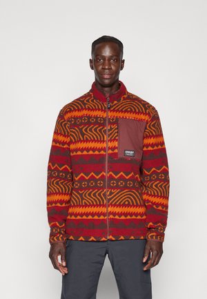 Rote, orange und braune gemusterte Fleecejacke mit einem Reißverschluss vorne und hohem Kragen. Verfügt über eine Brusttasche mit einem Markenpatch. Strukturiertes Design.
