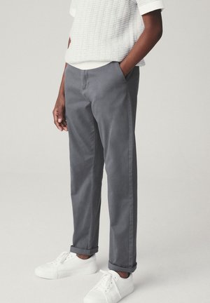 Pantalon en coton gris à coupe décontractée, deux poches avant et ourlets retroussés. Associé à des baskets blanches et un haut blanc texturé.