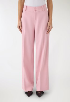 Pantaloni rosa a vita alta e gamba larga con doppio bottone indossati con top bianco e scarpe nere con punta a punta, mostrati dalla vita ai piedi.