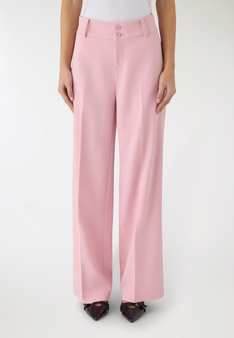 Pantaloni rosa a vita alta e gamba larga con doppio bottone indossati con top bianco e scarpe nere con punta a punta, mostrati dalla vita ai piedi.