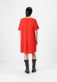 Vestido vermelho, folgado, com mangas curtas. Tecido texturizado, corte até ao joelho. Usado com botas castanhas até ao joelho com detalhes em fivela.