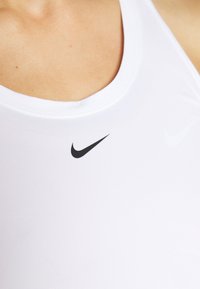 Primo piano di una persona che indossa una canotta sportiva bianca della Nike con il logo swoosh nero centrato sul petto.