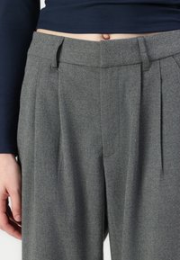 Calças de lã cinza com um corte ajustado, pregas frontais e uma textura suave. Inclui uma cintura média e bolsos laterais.