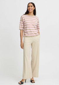Gestreifter Kurzarmpullover in Rosa und Beige, kombiniert mit cremefarbenen weiten Hosen und schwarzen Absatzsandalen. Glatter, weicher Stoff.