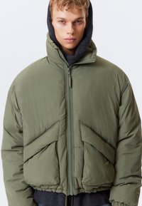 Grüne Steppjacke mit hohem Kragen, Reißverschluss und schrägen Vorderentaschen. Verfügt über ein kurzes Design und weichen, strukturierten Stoff.