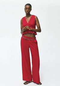 Rdeča brezrokavna majica s širokim robom, v kombinaciji z rdečimi širokimi hlačami z elastičnim pasom in okrasnim pasom.