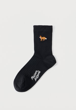 Șosetă neagră cu dungi, cu o vulpe portocalie brodată aproape de margine și text alb „Maison Kitsuné” pe talpă.