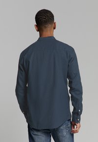 Marine blauwe langemouwen shirt, gemaakt van een gladde stof, met een button-down kraag en subtiele kromming aan de zijkanten. Met knopen bevestigde mouwen zichtbaar.