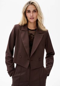 Brązowa krótka marynarka o podwójnym zapięciu, z wyciętymi klapami i dopasowanym krojem, z dwoma guzikami i gładką teksturą materiału.