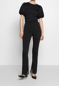 Top nero a maniche puff abbinato a pantaloni neri aderenti con spacchi laterali. Il top ha una trama liscia, mentre i pantaloni sono su misura.