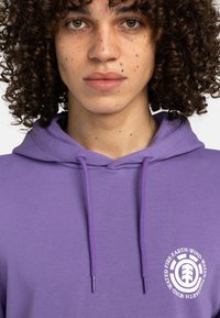 Purple hoodie with a front logo featuring circular text and tree design. Made of smooth fabric; includes drawstrings and a relaxed fit.