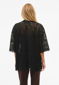 Czarny koronkowy kimono z szerokimi rękawami, ozdobione kwiatowymi wzorami i falistymi brzegami. Przezroczysta faktura, luźny krój.