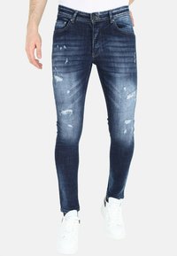 Vervaagde donkerblauwe jeans met een slim fit, met gescheurde details en subtiele wassing. Gepaard met witte sneakers.