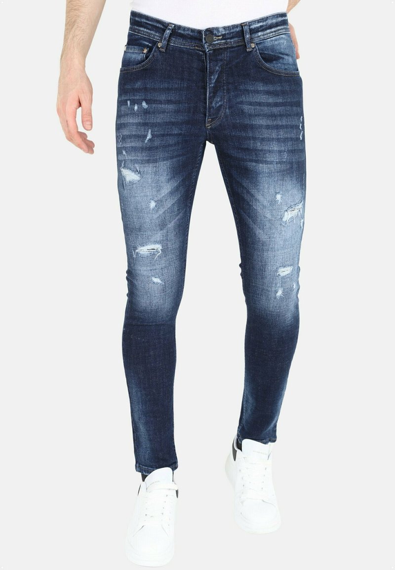 Vervaagde donkerblauwe jeans met een slim fit, met gescheurde details en subtiele wassing. Gepaard met witte sneakers.