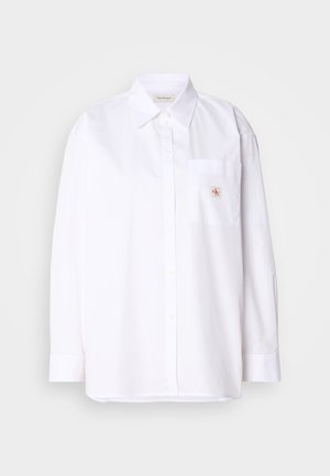 White cotton button-up shirt with long sleeves, a chest pocket, and a small CK logo patch on the pocket. Smooth texture and tailored fit.