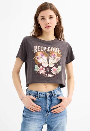 Camiseta corta gris hecha de una tela suave que presenta un gráfico de mariposa, acentos florales y el texto "MANTEN LA CALMA Y SIGUE ADELANTE" en letras coloridas.