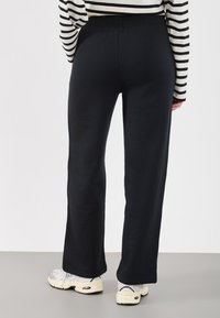 Czarne spodnie o prostych nogawkach z elastycznym pasem, zestawione z białymi sneakersami o fakturowanym wzorze i beżową podeszwą.