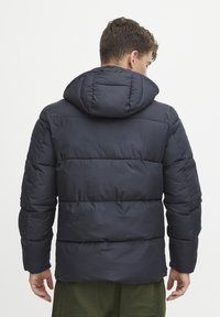 Marineblå pufferjakke med quiltet design og hette. Har en ensartet tekstur og er laget av et lett, varmt materiale.