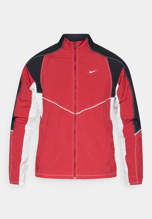 Rdeča jakna z črnimi in belimi detajli, visokim ovratnikom, sprednjim zadrgo in logotipom Nike. Ima kontrastne panele in podrobnosti šivanja.