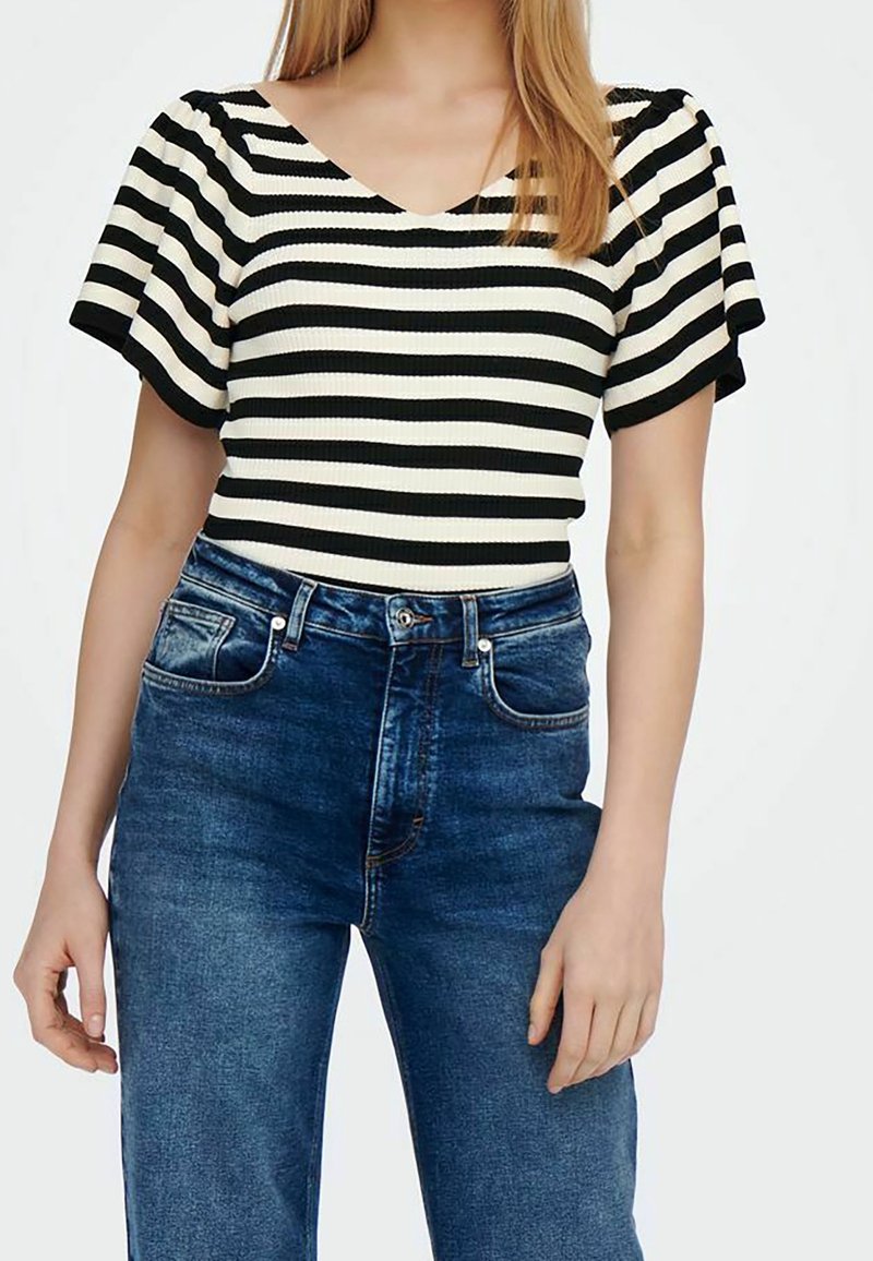 Haut à manches courtes à rayures noires et blanches avec un col en V, associé à un jean en denim bleu taille haute avec poches avant et une texture délavée.