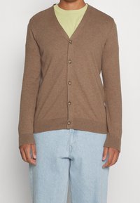Hnědý kardigan s výstřihem do V a dlouhými rukávy, zapínání na knoflíky, žebrované manžety a lem. Kombinovaný s světle modrými džíny. Měkká textura, volný střih.
