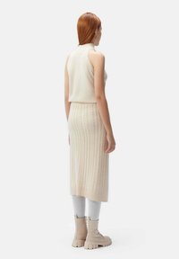 Stickad ärmlös topp i krämfärg, ihop med en lång ribbad kjol i krämfärg. Modellen bär grå leggings och beige ankelstövlar. Slät textur.