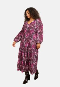 Dlouhá fialová šaty s abstraktním vzorem v růžové a bílé, véčkovým výstřihem, přítažným pasem, nafouklými rukávy a volánkovým lemem. Nosené s černými botami.