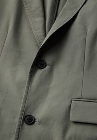 Blazer verde oliva con un diseño elegante, dos botones negros, solapas estructuradas y un detalle de bolsillo con textura de tela suave.