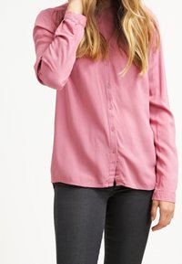 Chemise rose à manches longues avec boutons, en tissu lisse, dotée d'un col et de détails subtils froncés sur les épaules.