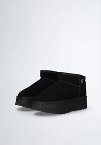 Stivaletti in suede nero con punta rotonda, suola piatta in gomma, cuciture minime e dettaglio con logo sul lato esterno.