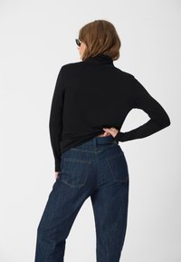 Black long-sleeve turtleneck top paired with high-waisted dark denim jeans, featuring a straight cut and subtle stitching.