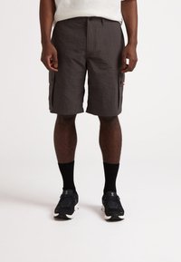 Shorts cargo en tissu gris foncé ; surface texturée ; deux poches latérales ; portés avec des chaussettes noires et des chaussures de sport noires.