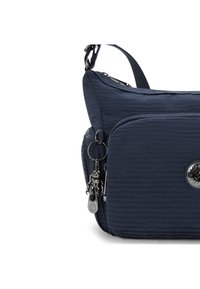 Borsa a spalla in blu navy con texture, dotata di tasca con zip frontale e portachiavi a forma di robot argentato attaccato al cursore della zip laterale.