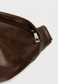 Καφέ δερμάτινο τσαντάκι μέσης με υφή, διακοσμημένο με ασημένιο μεταλλικό φερμουάρ και κομψό, κυρτό σχεδιασμό. Συμπαγές και λειτουργικό.