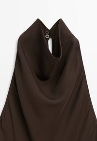 Top marrone scuro senza maniche con scollo drappeggiato chiuso sul retro da due bottoni su sfondo bianco.