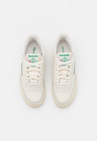 Baskets blanches Reebok avec logo vert et détail de feuille d'érable, design à lacets, et boîtier de l'orteil perforé, vues de dessus sur fond blanc.
