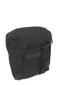 Bolso rectangular negro hecho de tejido duradero, con cierre de cremallera, correa ajustable y un parche de logo destacado en la parte frontal.
