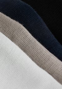 Detailný záber zložené pleteniny v bielych, béžových, námorníckych modrých a čiernych farbách, zobrazujúci textúru a detaily vzoru pletenia.