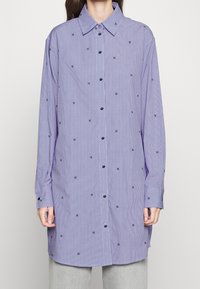 Lilla og hvidstribet langærmet skjorte med små broderede detaljer, knaplukning foran og klassisk krave.