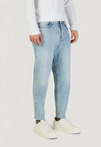 Vaqueros de mezclilla azul claro con un corte relajado, cintura de altura media, cierre frontal con cremallera, y diseño de cinco bolsillos, combinados con zapatillas blancas.